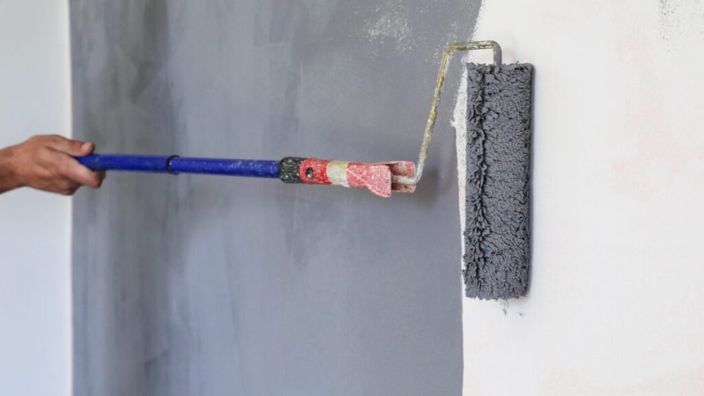 Paint roller applying grey paint over a white wall