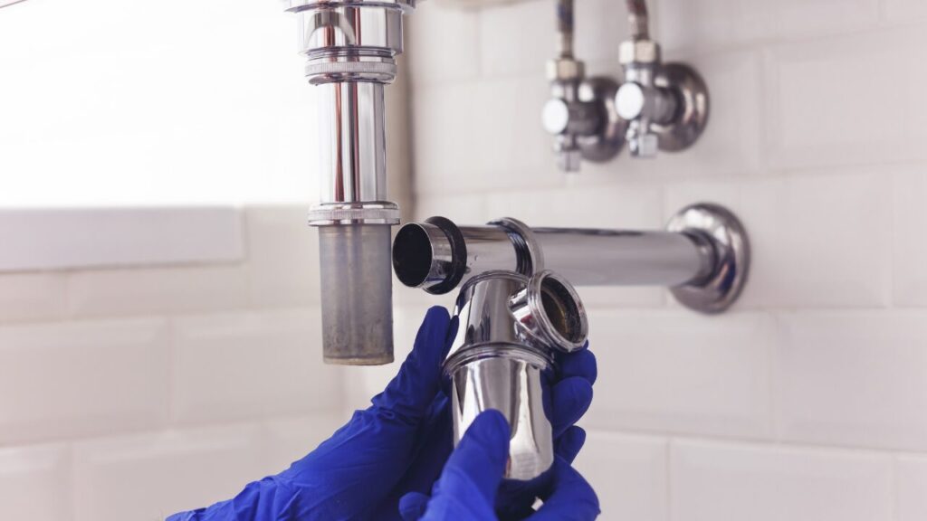 Plumber repairing a chrome siphon under a washbasin
