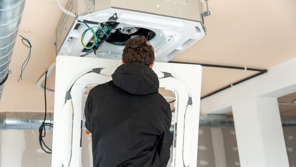 Technician installing a cassette air-conditioning unit in a ceiling