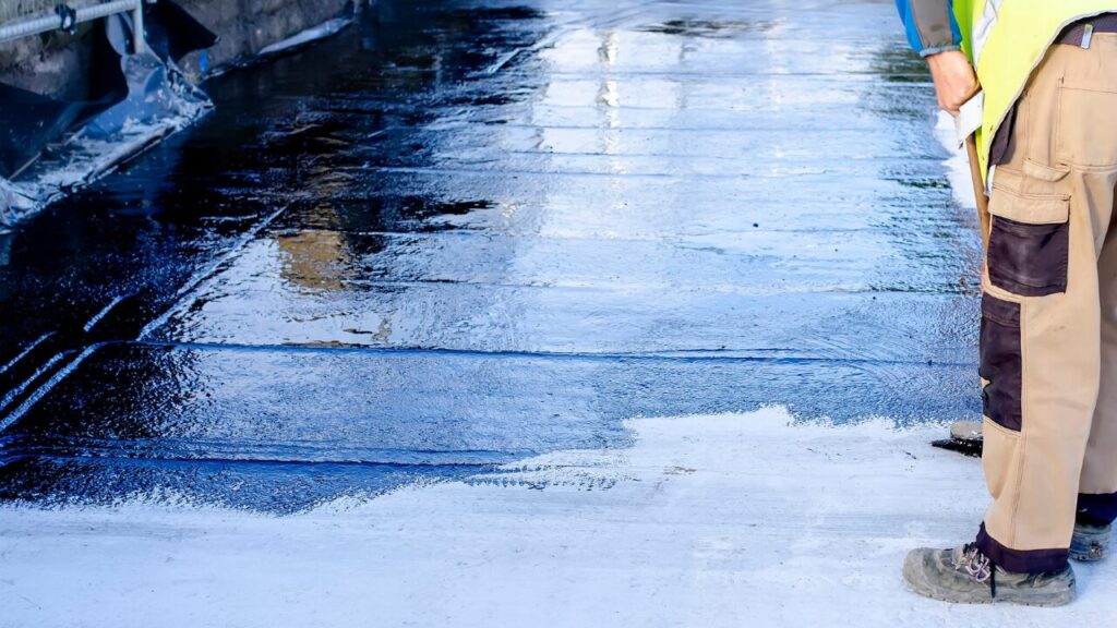 Builder applying bitumen waterproofing coating to concrete